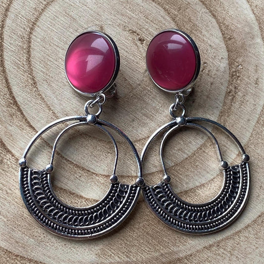 May include: A pair of silver clip on dangle earrings with pink glass stones. The earrings have a circular design with a detailed pattern.