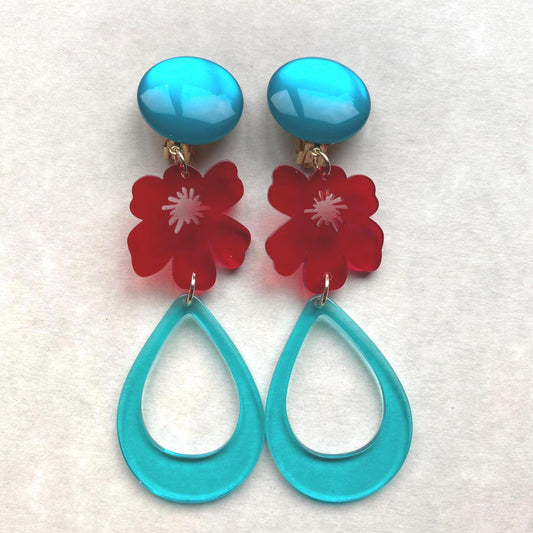 A pair of very large plastic clip on earrings in turquoise and red. Earrings feature a large turquoise clip, from which a red translucent flower and a turquoise teardrop dangle. Earrings are very large.
